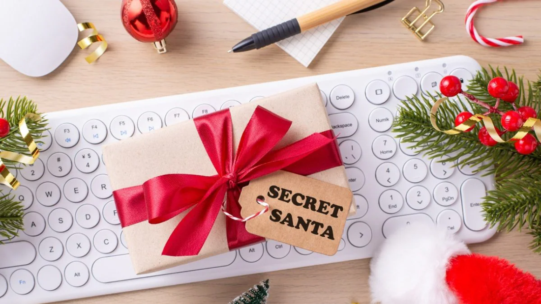 Secret Santa gift box with red ribbon on keyboard, Christmas decorations in office setting